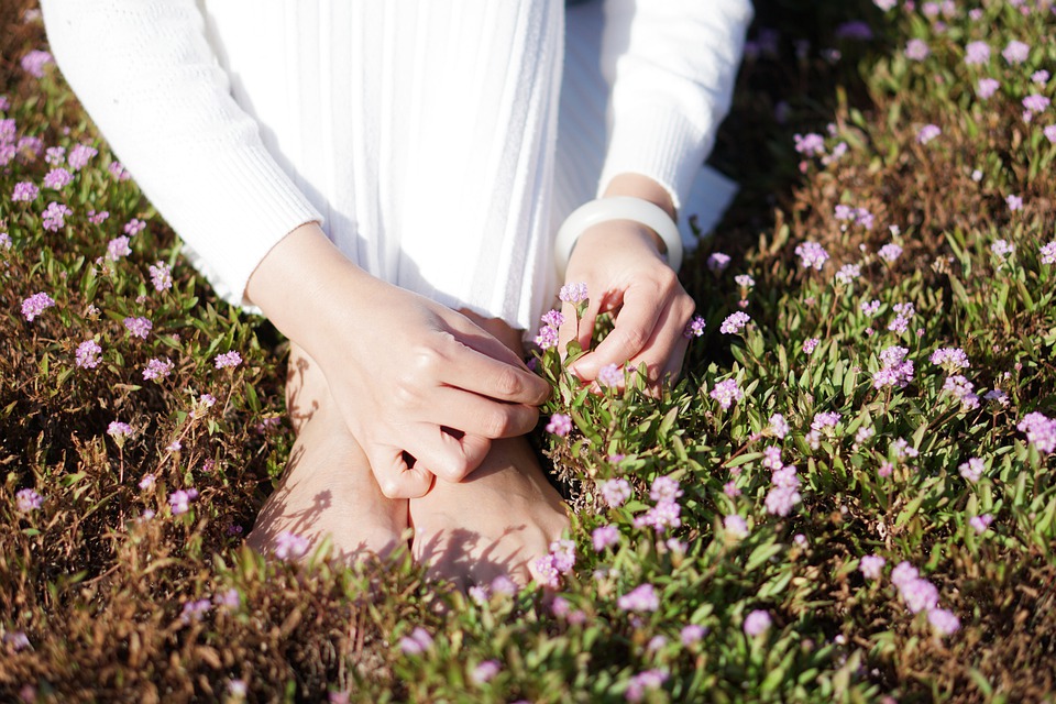 a woman sits on a meadow in a white dress and picks small pink flowers