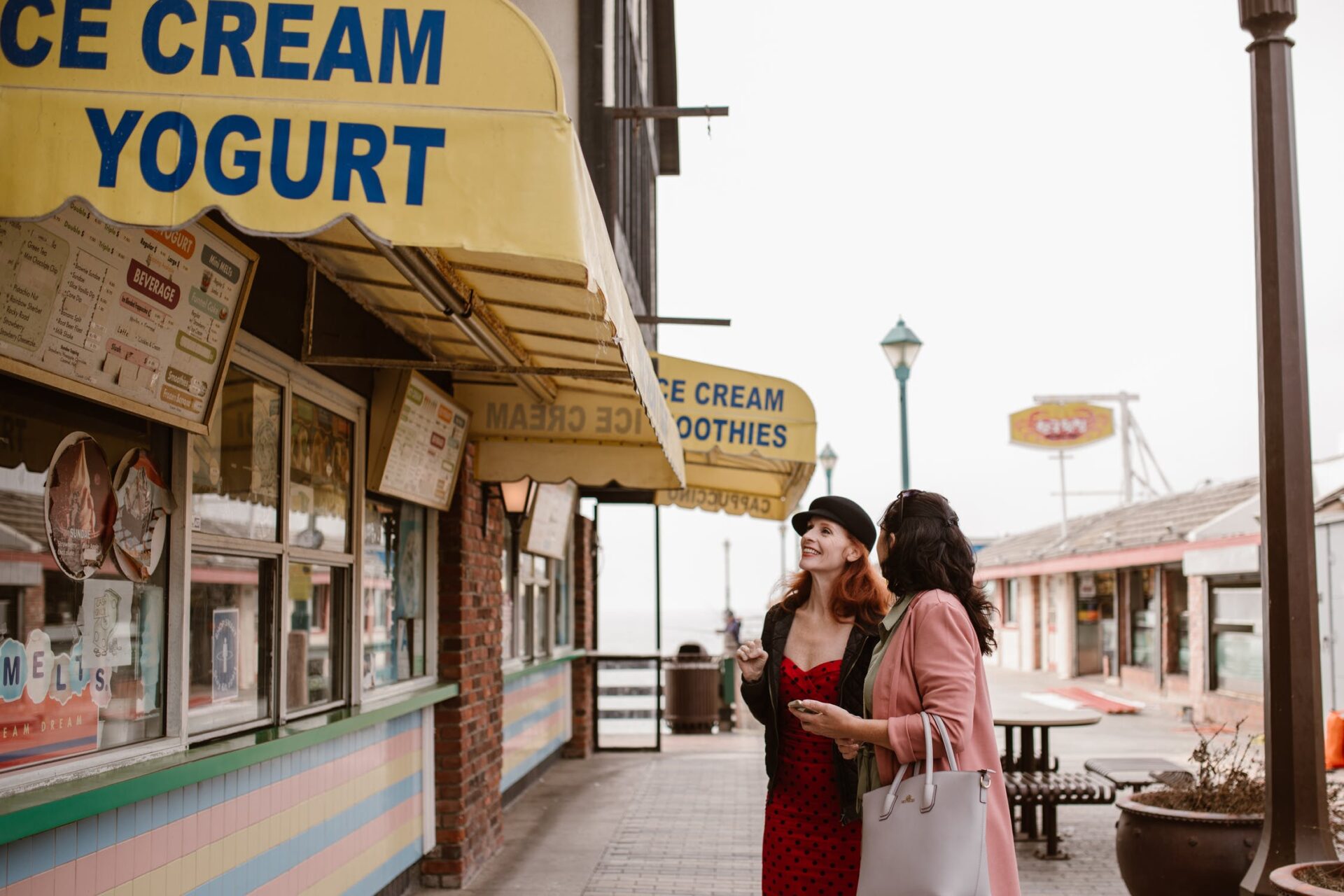 two women, who could be in the age of menopause, stand in front of an ice cream parlor and laugh