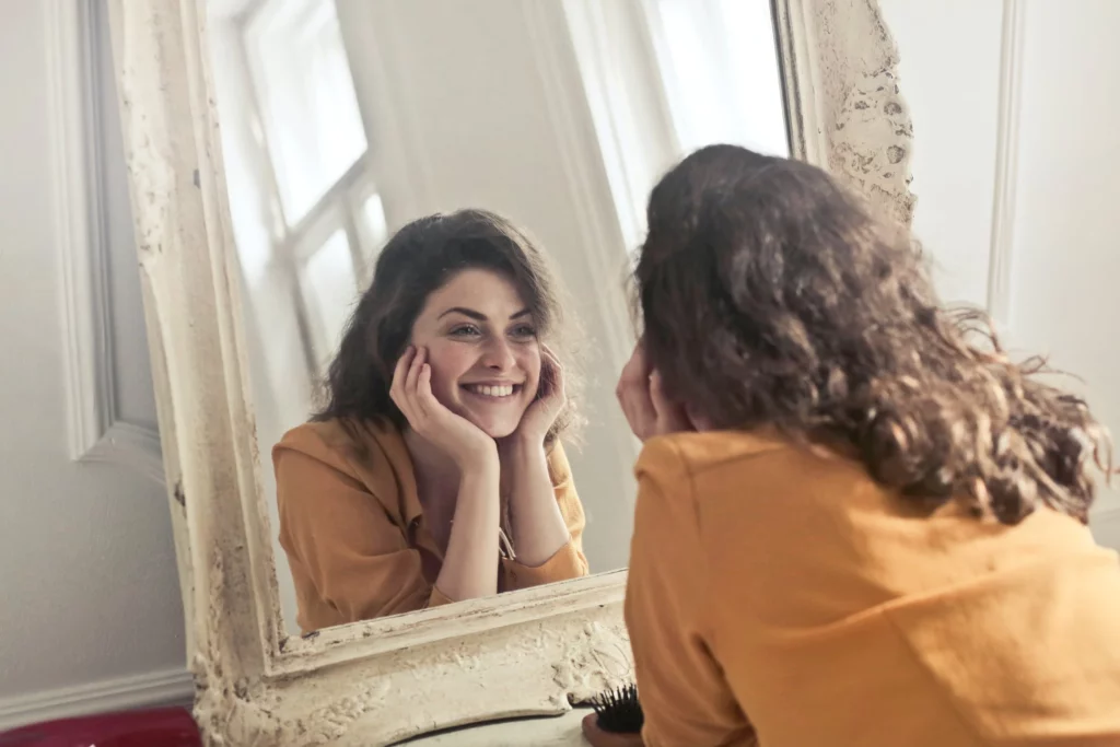 Frau lächelt glücklich in einen Spiegel