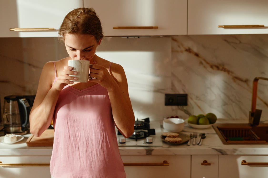 Woman standing leaning against kitchen counter drinking tea