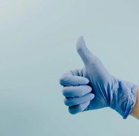 eine Hand in einem blauen OP-Handschuh zeigt den Daumen nach oben