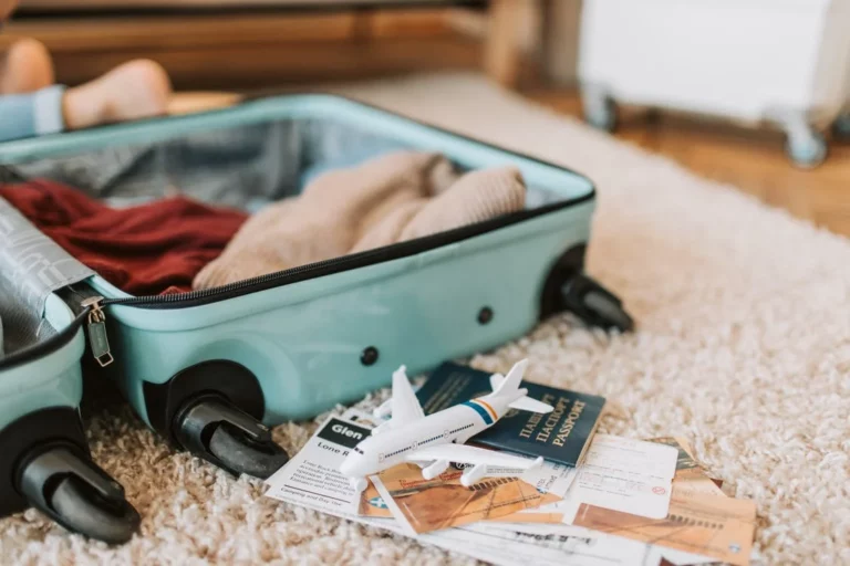 ein offener Koffer liegt auf dem Boden, davor liegen Reisedokumente und ein kleines Spielzeugflugezug