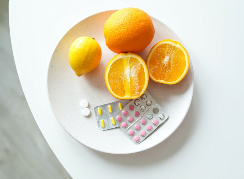 Vitaminpräparate in Kapselform in der Verpackung auf einem Teller zusammen mit Orangen und einer Zitrone
