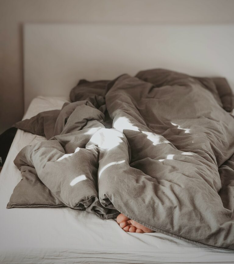 One person lies in bed under blanket, only foot looks out