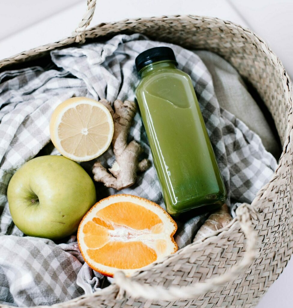 green fruit juice or smoothie in a basket with apple, half orange and half lemon and checkered blanket