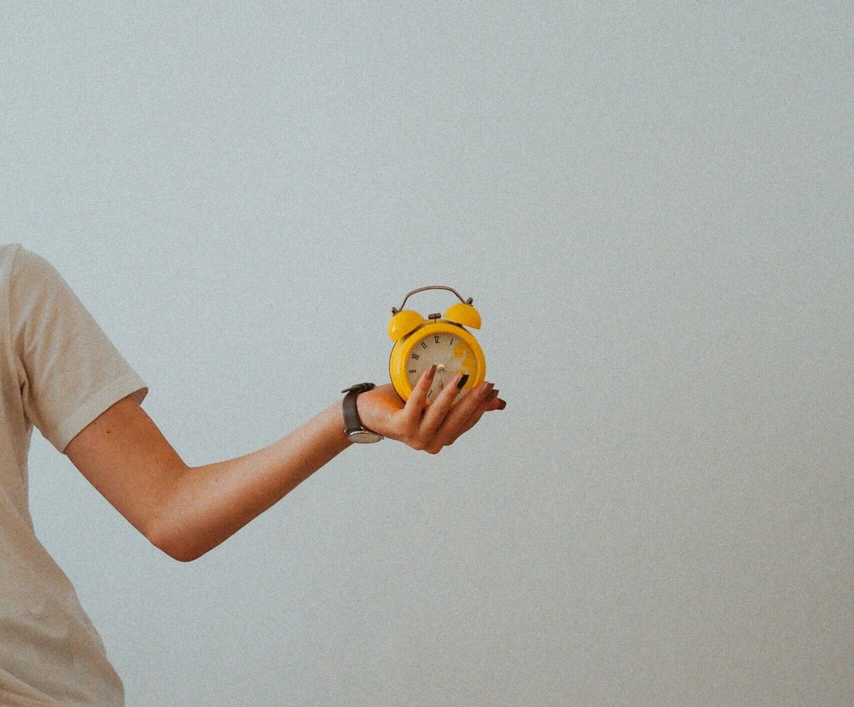 Woman holding yellow analog alarm clock in hand
