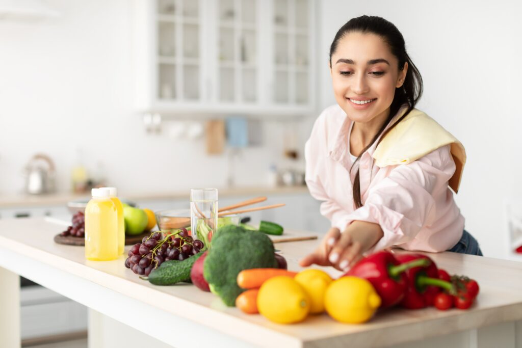 woman reaches for lemon - peppers and other fruit and vegetables on the worktop