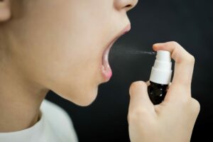 sprayflasche Zimply Natural wird in den Mund gesprüht Frau drückt auf Pumpzerstäuber vor schwarzem Hintergrund