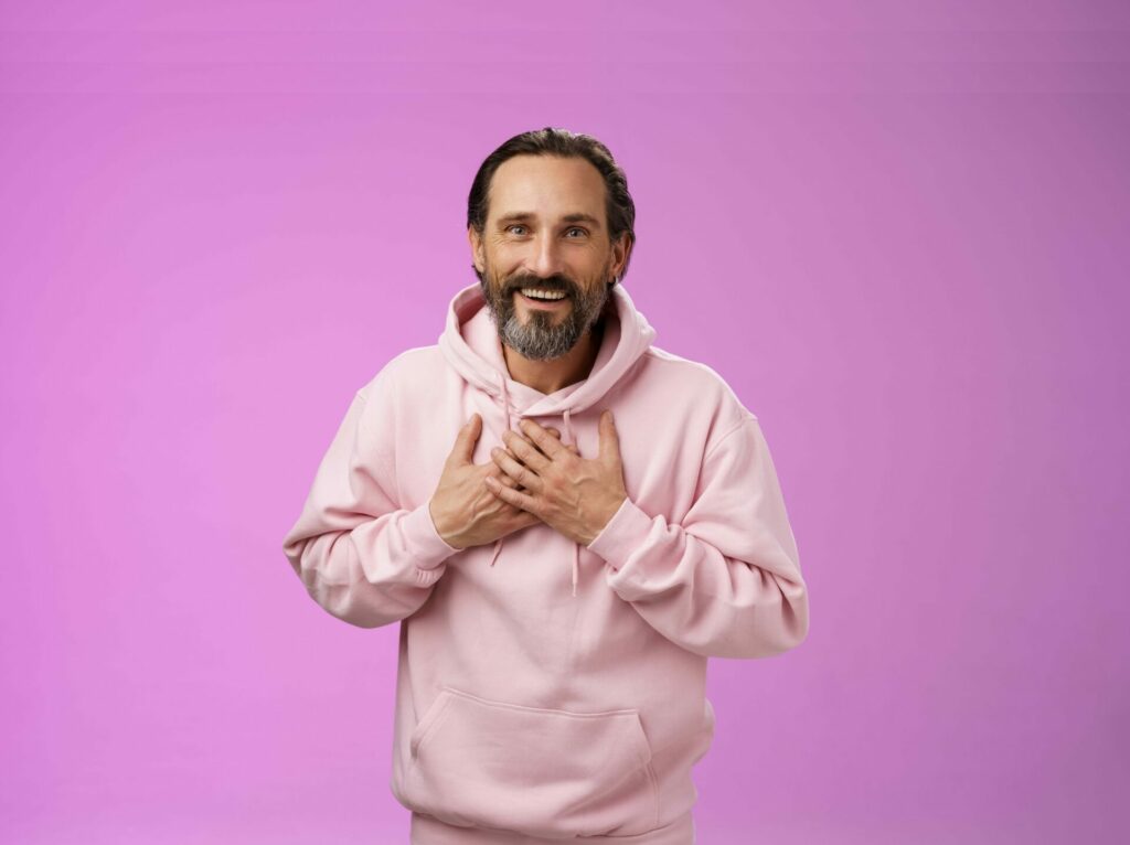 Mann mit rosa Pulli vor Rosa Wand fasst sich auf die Brust und ist erleichtert, dass sein sodbrennen weg ist durch pflanzliche Hilfe von Zimply Natural