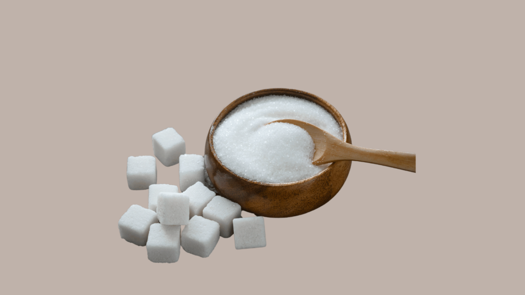 A wooden bowl filled with sugar and wooden spoon on brown background and sugar cubes next to it.
