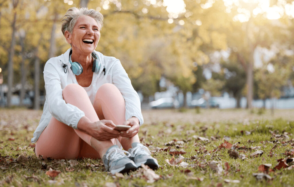 Ältere Frau sitzt lachend auf einer Wiese