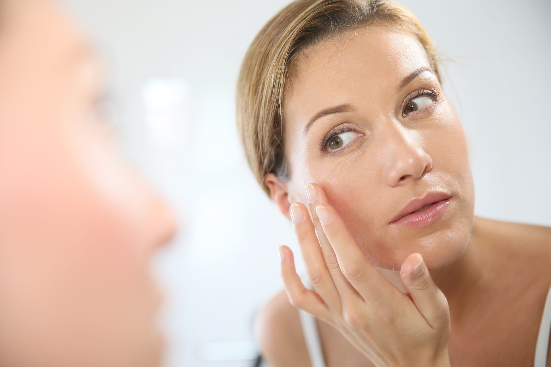 Woman looks at herself in the mirror and strokes her cheek with her finger.