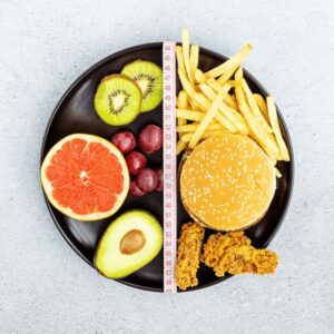 Plate with food separated in the middle. On one side is fruit and vegetables, on the right is fast food.
