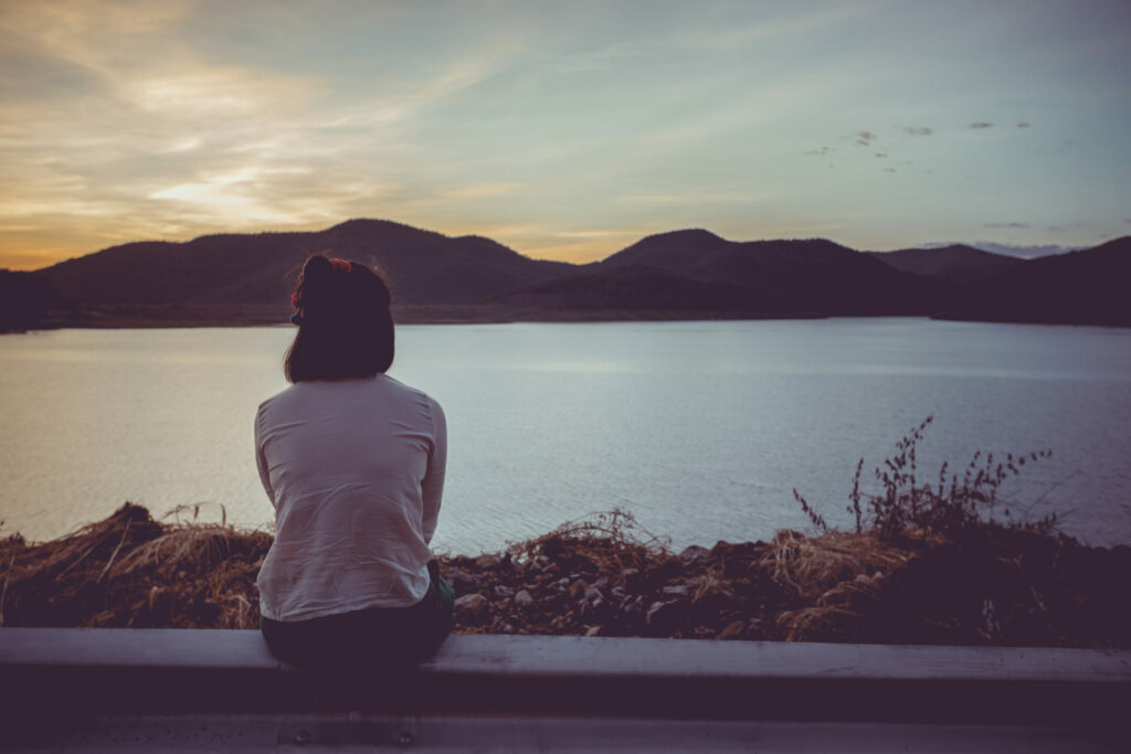 Woman sitting in front of a lake/sea and looking into the distance