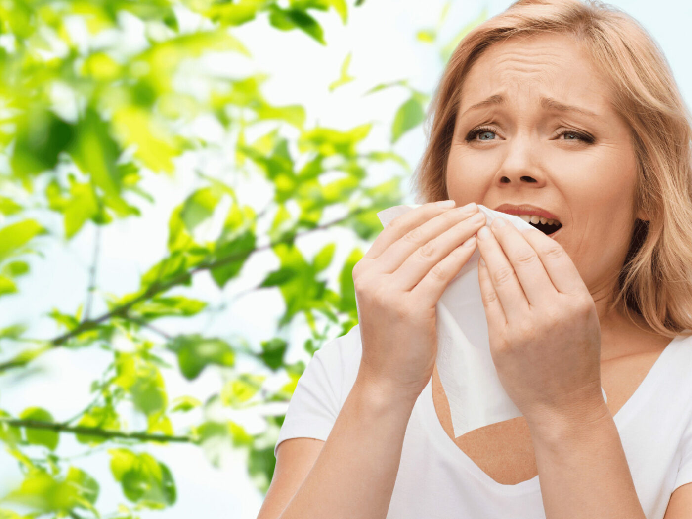 Woman sneezing in front of tree with handkerchief in hand