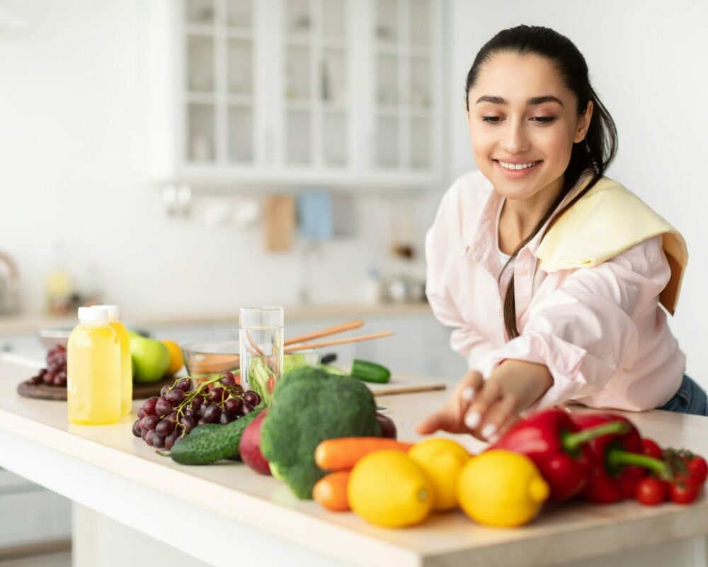 woman reaches for lemon - peppers and other fruit and vegetables on the worktop