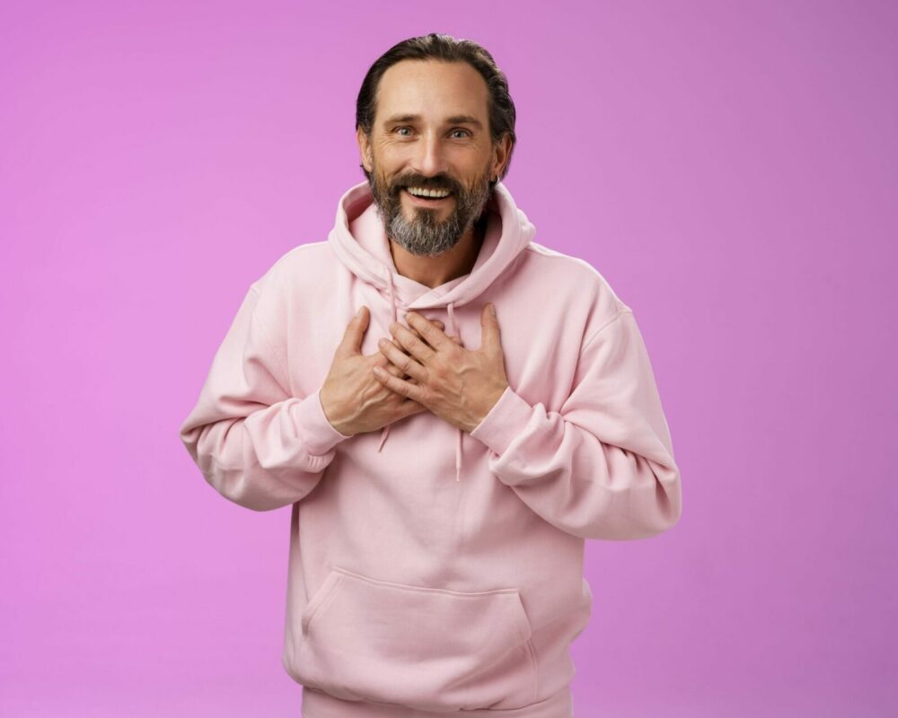 Mann mit rosa Pulli vor Rosa Wand fasst sich auf die Brust und ist erleichtert, dass sein sodbrennen weg ist durch pflanzliche Hilfe von Zimply Natural