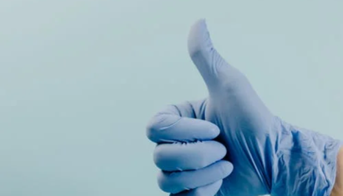 one hand in a blue surgical glove shows the thumb upwards